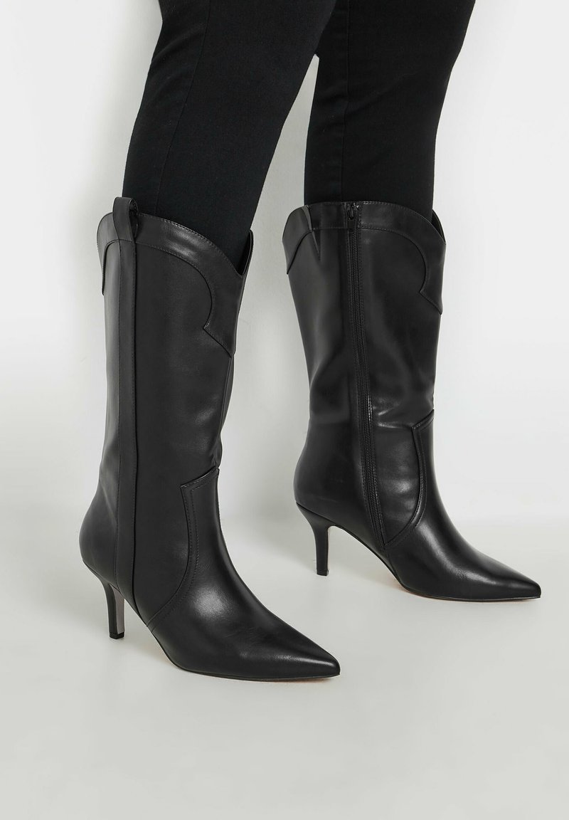 Mustat nahka nilkkurit, joissa on teräväkärkiset varvat ja kapeat korot. Ominaisuuksiin kuuluu sileä pinta ja koristeellinen tikkaus yläreunassa.