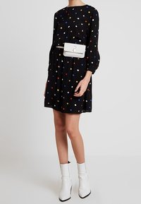 Czarna sukienka w wielokolorowe kropki, z długimi rękawami, podkreśloną talią i białą torbą biodrową; zestawiona z białymi botkami na kostkę.