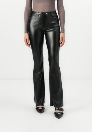 Black faux leather flared pants with front pockets, a button closure, and a smooth, shiny texture. Worn with pointed black heels and ankle straps.