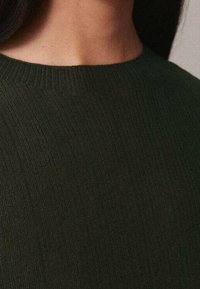 Haut en maille côtelée vert foncé avec un col rond. Texture lisse et coupe ajustée autour des épaules et du cou.