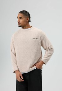 Fleece pullover in lichtbeige, met een gestructureerd oppervlak, lange mouwen en een ronde halslijn. Kleine zwarte logo op de linkerborst.