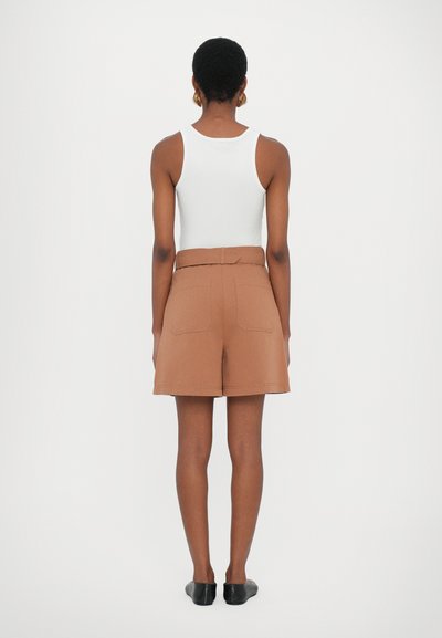 Shorts marron avec ceinture, équipés de deux poches arrière, associés à un débardeur blanc. Le tissu semble lisse et les shorts ont une coupe structurée.