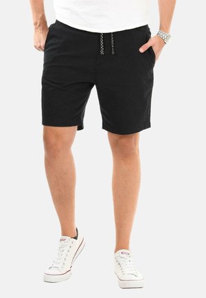 Black shorts made of soft fabric, featuring a drawstring waistband, side pockets, and a relaxed fit. Worn with white sneakers.