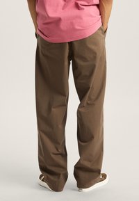 Brown cotton pants with a relaxed fit, featuring a smooth texture and a straight leg design. Worn with white sneakers.