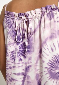 Haut en tie-dye lilas avec un col froncé, des bretelles réglables et des liens décoratifs à l'arrière. Il est composé d'un tissu doux et fluide et d'un mélange de couleurs.