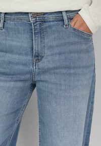 Jasnoniebieskie dżinsy z denimu o prostym kroju, z pojedynczym zapięciem na guzik, przednimi kieszeniami i subtelnym blaknięciem. Teksturowana tkanina z widocznymi szwami.