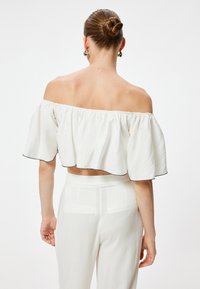 Top bianco smussato sulla spalla con maniche arricciate e design cropped, con bordi neri, abbinato a pantaloni bianchi a vita alta.