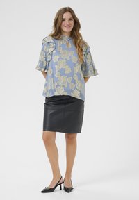 Modra cvetna bluza z naborki na rokavih, z odprtim vratnim izrezom; v kombinaciji z črno usnjeno krilom in črnimi slingback petkami.