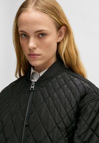 Giacca bomber nera trapuntata con colletto alto e chiusura a zip, caratterizzata da una superficie tessurizzata e una silhouette aderente.
