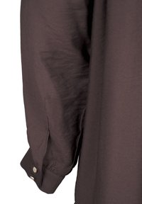 Poignet de chemise à manches longues de couleur brun foncé avec deux boutons argentés sur le poignet, présenté sur un fond blanc.