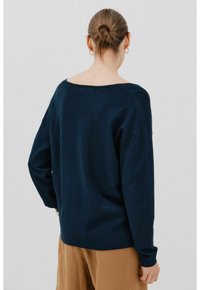 Marineblaue Langarm-Sweatshirt mit weitem Halsausschnitt, strukturiertem Stoff und lockerer Passform, kombiniert mit hellbraunen Hosen.
