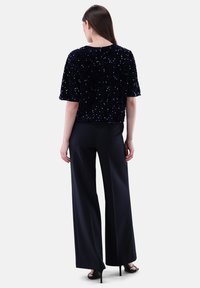 Schwarzes Pailletten-Top mit kurzen Ärmeln und Rundhalsausschnitt, kombiniert mit hochgeschnittenen dunklen Hosen und offenen Schuhen mit Absatz. Glatte, glänzende Textur.