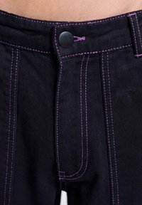 Jean en denim foncé avec des coutures violet vif et une fermeture bouton noir à la taille.