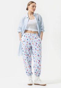 Chemise rayée bleu clair sur un débardeur blanc, associée à un pantalon de pyjama à motifs avec des impressions colorées de macarons. Comprend des poches et un cordon de serrage.