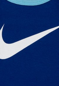 Un tissu en coton bleu présente un logo Nike Swoosh blanc bien en évidence, avec un col côtelé bleu clair. La surface semble lisse et texturée.
