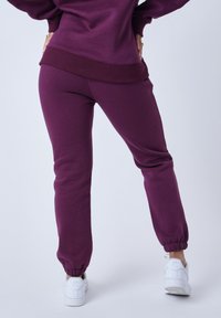 Pantalones jogger burdeos con puños acanalados, que presentan una textura suave y un ajuste casual. Combinados con zapatillas blancas para crear contraste.
