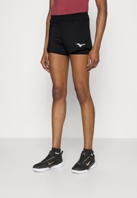 Pantalones cortos atléticos negros con una cinturilla ajustada, bolsillos laterales y un logo blanco a la izquierda. Combinados con zapatillas deportivas en blanco y negro.