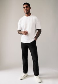 Camiseta blanca de manga corta combinada con pantalones negros y zapatillas blancas. La camiseta tiene un cuello redondo y el conjunto presenta un ajuste casual.