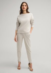Light gray sweatshirt with a round neck and long sleeves paired with matching fitted pants; features smooth texture and subtle seams. Gold high-heeled sandals.