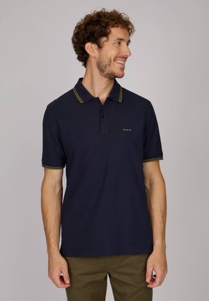 Polo shirt bleu marine avec un tissu texturé, présentant des rayures accent jaune-vert sur le col et les manches, ainsi qu'un détail de logo subtil.