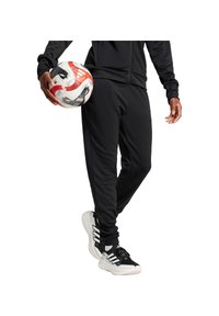 Schwarze Sporthosen mit schmaler Passform, kombiniert mit schwarz-weißem Sportschuh. Ein rot-weißer Fußball wird in der linken Hand gehalten.
