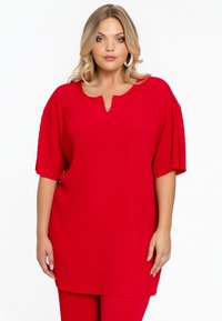 Rode geribbelde tuniek met korte mouwen en een ronde halslijn met een keyhole detail. Gecombineerd met bijpassende rode broek.