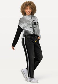 Suéter gris y negro con estampado gráfico, combinado con pantalones negros con rayas laterales y cordón. Zapatillas blancas completan el look.