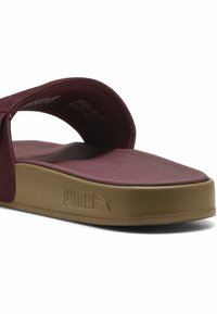 Maron farvet slidesandal med en rund overdelsrem, struktureret fodseng og tan farvet ydersål med et Puma-logo præget på siden.