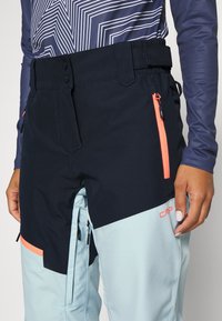 Skidbyxor med en svart och ljusblå färgpalett, justerbar midja, framfickor och kontrasterande orangea dragkedjor för extra detalj.