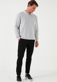 Camisa de polo de manga larga en gris claro con cuello abotonado; combinada con pantalones negros ajustados y zapatillas negras con detalles texturizados.