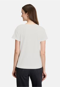 Hvid kortærmet t-shirt med rund halsudskæring, der har en afslappet pasform og blød tekstur, båret med mørke jeans.