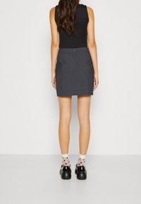 Haut sans manches noir associé à une jupe gris foncé. La jupe a une fermeture éclair, et le mannequin porte des chaussettes à motifs avec des chaussures noires.