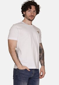 T-shirt bianco in cotone con maniche corte e scollatura rotonda. Presenta un piccolo design ricamato in oro sul lato sinistro del petto.