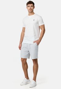 T-shirt blanche à manches courtes avec un col rond et un petit emblème, associée à un short en grès clair texturé et des baskets blanches.