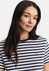 Young woman with long dark hair wearing a navy and white striped shirt, facing front with a slight smile on a plain white background.