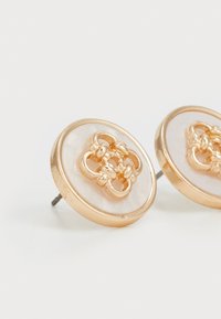 Boucles d'oreilles en métal doré de forme circulaire, avec un noyau lisse de couleur claire et des détails en métal complexes au centre.