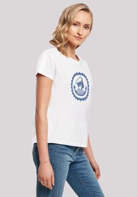 Weißes Baumwoll-T-Shirt mit kurzen Ärmeln, ausgestattet mit einem blauen, runden Grafikdesign eines Ankers und Streifen auf der Vorderseite. Lässiger Schnitt.