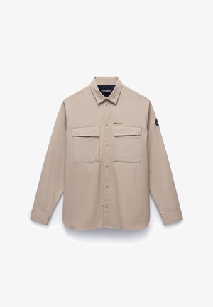 Beige långärmad skjorta i lätt tyg, med knäppning fram, två bröstfickor och en liten logotyp-patch på ärmen.