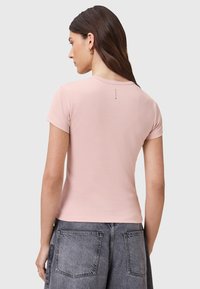 Lichtroze aansluitend t-shirt met korte mouwen, ronde hals, gladde katoenstof en een klein logo-tag aan de achterkant. Gecombineerd met grijze spijkerbroek.