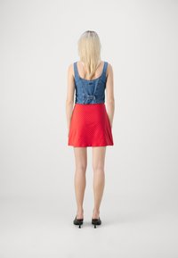 Denim crop top hátul övvel, piros, fehér pöttyös, bővülő szoknyával párosítva. A modellen fekete, sarkú mules cipők vannak.