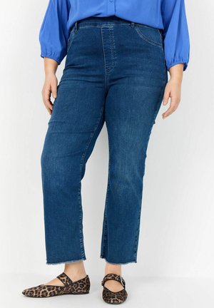 Jeans de mezclilla azul con cintura alta y diseño de pierna recta; presentan un dobladillo sin terminar, combinados con bailarinas de estampado de leopardo.