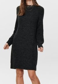 Abito maglione nero in maglia, con maniche lunghe, scollatura rotonda e texture a coste. Lunghezza fino a metà coscia con fessure laterali per facilitare i movimenti.