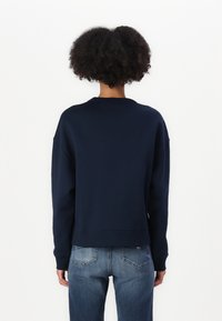 Felpa blu navy con collo a giro, maniche lunghe e vestibilità relaxed; abbinata a jeans azzurri con tasche posteriori.