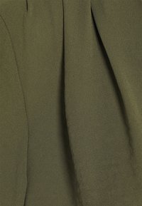 Tessuto verde oliva con una superficie tridimensionale e morbide pieghe che creano ombre e profondità sottili.