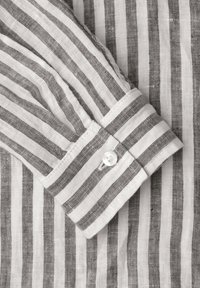 Langärmelige Manschette eines gestreiften weißen und grauen Leinenhemds mit einem einzelnen weißen, befestigten Knopf.