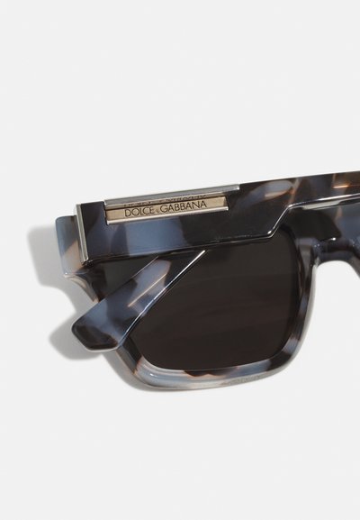 Ochelari de soare cu model țestoasă, dimensiuni geometrice, lentile întunecate și o bară accent de argint cu numele brandului "Dolce & Gabbana."