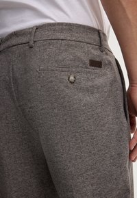 Graue Textilhose mit schmaler Passform, mit einer Gesäßtasche, Knopfschluss und einem Lederschild mit Logo am Bund.