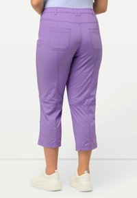 Pantalons courts lilas clair avec taille élastique, deux poches arrière et détails de couture visibles. Associés à des baskets blanches.