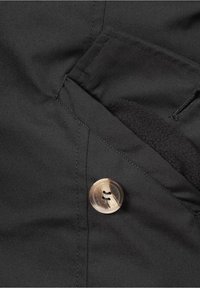 Chaqueta de tela negra con un acabado texturizado, que presenta un botón redondo marrón y un borde de bolsillo con forro de forro polar.