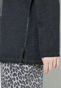 Camisa negra de manga larga con detalle de dobladillo dividido, hecha de una tela suave, combinada con pantalones gris claro que presentan un estampado de leopardo.